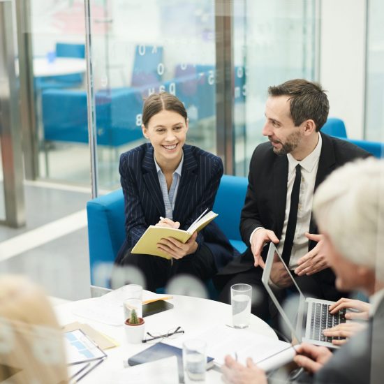 Group of cheerful business people discussing project sitting at coffe table during meeting, shot from behind glass, copy space